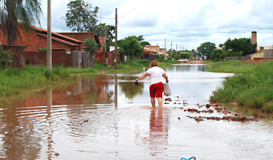 Com as águas na canela, dona Tânia atravessa a "Lagoa do Santo André" em direção à sua casa