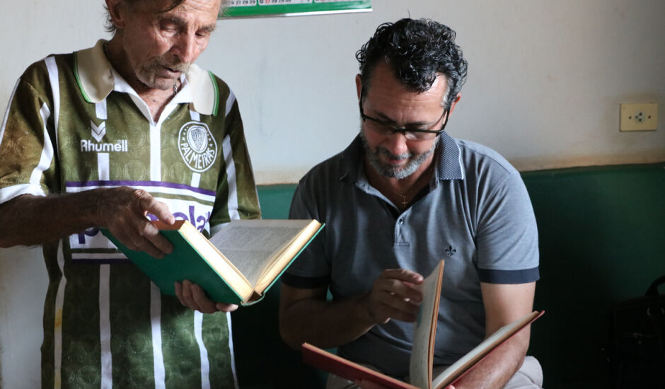 Idoso José Moreira (à esquerda) entrega livro para diretores de escolas