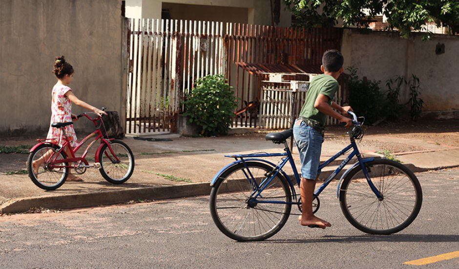 De bicicleta, duas crianças são vistas em uma rua de Três Lagoas; um a espera do outro na manhã ensolarada desta sexta-feira